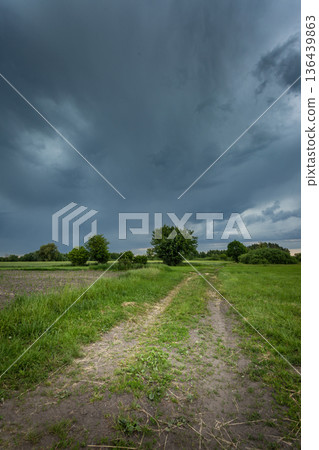Dark storm cloud over meadow with road 136439863