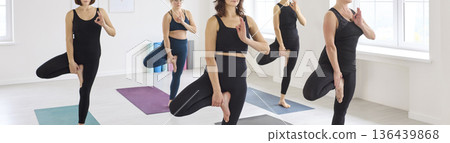 Women's yoga group balancing in standing quad stretch during class in studio Women's yoga group balancing in standing quad stretch during class in studio 136439868