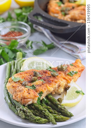 Delicious haddock fish piccata, battered fish fillet with capers, lemon and asparagus, vertical Delicious haddock fish piccata, battered fish fillet with capers, lemon and asparagus, vertical 136439995