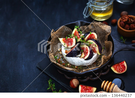 Camembert or brie cheese with fresh figs walnuts and honey on iron frying pan, over dark background Camembert or brie cheese with fresh figs walnuts and honey on iron frying pan, over dark background 136440237