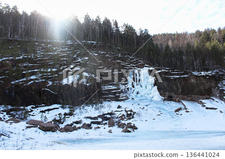 Winter landscape of Krasnoyarsk Stolby national park with frozen waterfall and snow-covered forest mountain. Natural beauty and extreme tourism. A formerly used granite quarry. 136441024