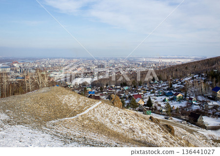 Aerial view of a diverse cityscape nestled between hills and snowy slopes with scattered houses. Urban and rural landscape in winter season. 136441027