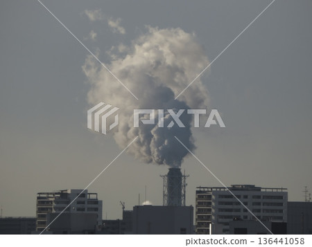 A view of white factory smoke rising into the winter sky and city buildings 136441058
