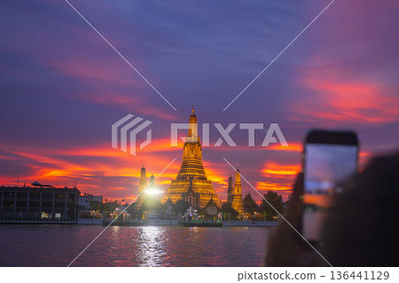 Tourists take photos with their smartphones at Wat Arun Ratchawararam Ratchaworamahawihan during sunset in Bangkok, Thailand. 136441129