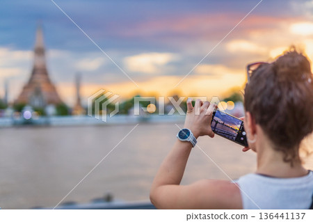 Tourists take photos with their smartphones at Wat Arun Ratchawararam Ratchaworamahawihan during sunset in Bangkok, Thailand. 136441137