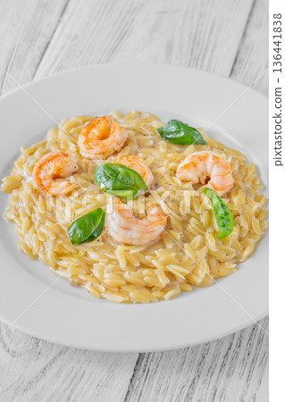 Creamy orzotto pasta topped with grilled prawns and fresh basil on rustic wooden table 136441838