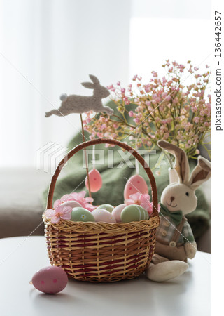 Easter Basket with Ester Eggs, Plush Bunny and Spring Decor on White Table intoCozy Living Room Easter Basket with Ester Eggs, Plush Bunny and Spring Decor on White Table intoCozy Living Room 136442657