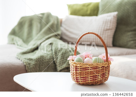 Easter Basket with Ester Eggs, Plush Bunny and Spring Decor on White Table intoCozy Living Room Easter Basket with Ester Eggs, Plush Bunny and Spring Decor on White Table intoCozy Living Room 136442658