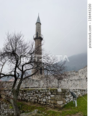Stone minaret rising inside the historic Travnik Fortress with old walls and bare trees. Cloudy winter atmosphere highlighting Ottoman heritage and medieval architecture Stone minaret rising inside the historic Travnik Fortress with old walls and bare trees. Cloudy winter atmosphere highlighting Ottoman heritage and medieval architecture 136443200