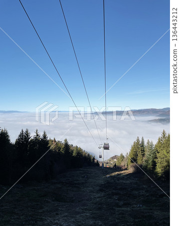 Cable car descending above a sea of clouds near Sarajevo with forested slopes and mountains in the distance. Winter travel scene with dramatic foggy landscape 136443212