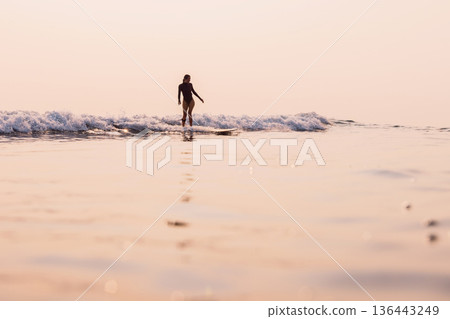 Woman on longboard riding on small wave with warm sunrise . 136443249