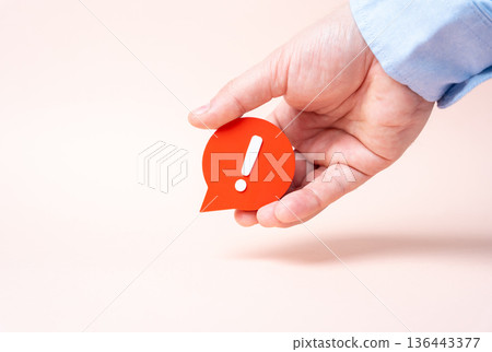 A hand holds a comment with an exclamation mark. A harsh comment, a sharp reaction. A complaint and dissatisfaction. Feedback culture shapes reputation, crisis response, and brand trust. 136443377