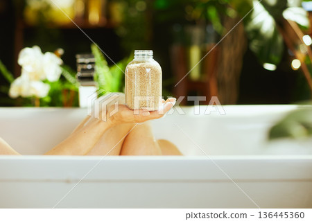 Hand Holding Bath Salts in Relaxing Tub 136445360