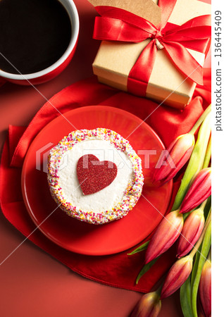 Valentine's Day festive red background. Cake with red heart, cup of coffee, gift box and spring red tulip flower bouquet. Top view Valentine's Day festive red background. Cake with red heart, cup of coffee, gift box and spring red tulip flower bouquet. Top view 136445409
