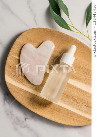 Rose quartz gua sha tool and oil bottle on wooden tray, face massage tool, beauty abstract photo. Copy space Rose quartz gua sha tool and oil bottle on wooden tray, face massage tool, beauty abstract photo. Copy space 136445416