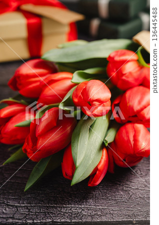 Red tulip bouquet with gift boxes. Easter or birthday holiday black background. Red tulip bouquet with gift boxes. Easter or birthday holiday black background. 136445488