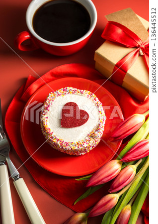 Valentine's Day festive red background. Cake with red heart, cup of coffee, gift box and spring red tulip flower bouquet. Top view Valentine's Day festive red background. Cake with red heart, cup of coffee, gift box and spring red tulip flower bouquet. Top view 136445512