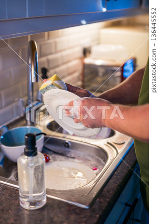 A man washing dishes in the kitchen, home chores, daily routine A man washing dishes in the kitchen, home chores, daily routine 136445552