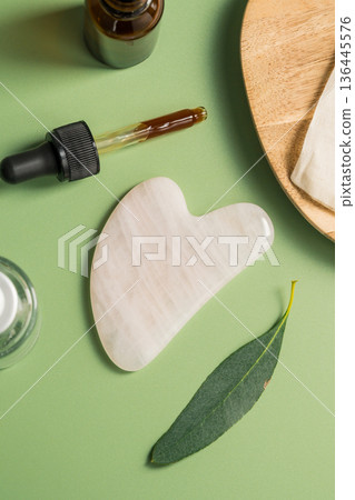 Rose quartz gua sha tool and oil bottle on wooden tray, face massage tool, beauty abstract photo. Copy space 136445576