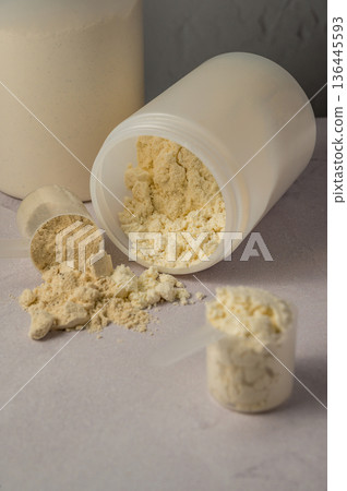 Protein powder in scoops with white plastic protein tubes, jars in background. Body building, muscle growth and food supplement concept 136445593