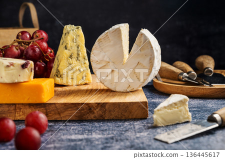 Different types of cheese on a board, served with grapes and dried fruits. 136445617