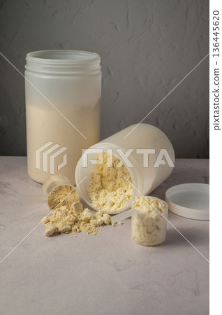 Protein powder in scoops with white plastic protein tubes, jars in background. Body building, muscle growth and food supplement concept Protein powder in scoops with white plastic protein tubes, jars in background. Body building, muscle growth and food supplement concept 136445620