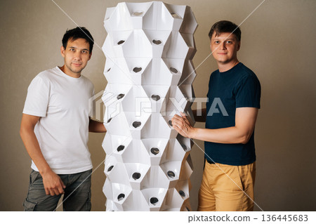 Portrait of male gardeners presenting vertical hydroponic tower, showcasing innovative urban farming technology supporting local sustainable agriculture and environmentally friendly growing methods. Portrait of male gardeners presenting vertical hydroponic tower, showcasing innovative urban farming technology supporting local sustainable agriculture and environmentally friendly growing methods. 136445683