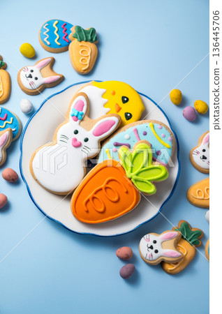 Easter holiday background with easter cookies in a plate: bunny, chick, carrot and egg on blue background, with mini chocolate egg candies Easter holiday background with easter cookies in a plate: bunny, chick, carrot and egg on blue background, with mini chocolate egg candies 136445706
