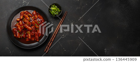 Traditional Korean tteokbokki served on black plate with chopsticks and sesame seeds on black rustic background, space for text 136445909