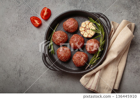 Raw meatballs with garlic and rosemary in cast iron pan on gray concrete background, copy space Raw meatballs with garlic and rosemary in cast iron pan on gray concrete background, copy space 136445910