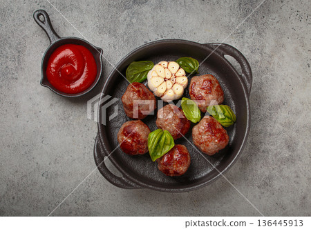 Delicious fried meatballs with basil, garlic in cast iron pan and tomato sauce top view 136445913
