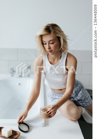Woman Get Cosmetic Body Scrub From Jar Sitting On Bath In Bathroom Woman Get Cosmetic Body Scrub From Jar Sitting On Bath In Bathroom 136448009