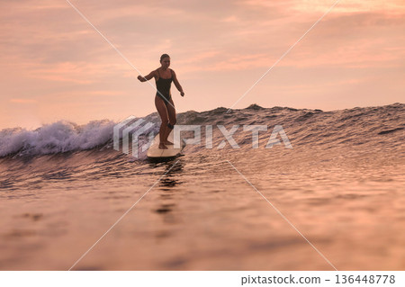 Relaxed Female Enjoying Peaceful Surfboard Ride During Sunset 136448778