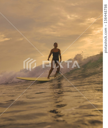 Graceful Female Surfer Enjoying Tranquil Sunset On Her Longboard Graceful Female Surfer Enjoying Tranquil Sunset On Her Longboard 136448786