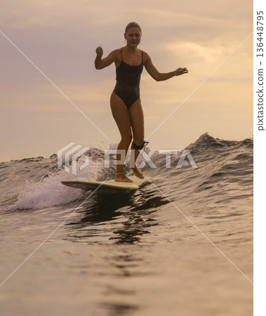 Captivating Sunset Surf Scene With Confident Woman And Tranquil Waters 136448795