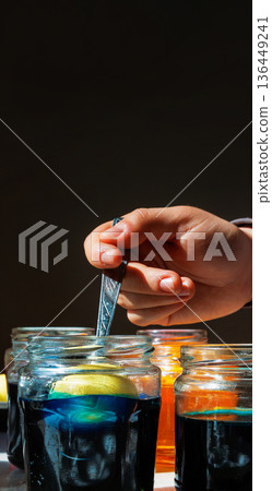 Vertical close up of a hand holding a spoon with an egg submerged in a blue food dye jar on dark background with copy space Vertical close up of a hand holding a spoon with an egg submerged in a blue food dye jar on dark background with copy space 136449241
