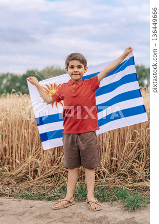Patriot Boy Standing In Wheat Field Holding Uruguayan Flag In The Wind, Uruguay Patriot Boy Standing In Wheat Field Holding Uruguayan Flag In The Wind, Uruguay 136449666