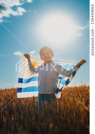 Patriot Boy Standing In Wheat Field Holding Uruguayan Flag In The Wind, Uruguay Patriot Boy Standing In Wheat Field Holding Uruguayan Flag In The Wind, Uruguay 136449668