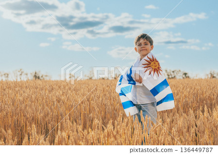 Patriot Boy Standing In Wheat Field Holding Uruguayan Flag In The Wind, Uruguay Patriot Boy Standing In Wheat Field Holding Uruguayan Flag In The Wind, Uruguay 136449787