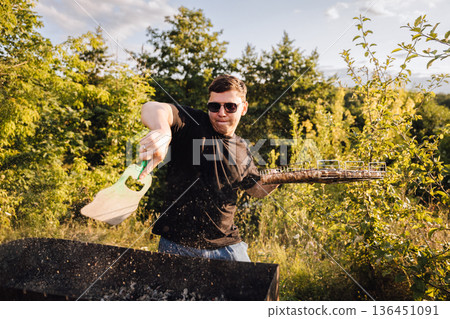 Man fanning charcoal grill outdoors at sunset, sparks flying during summer barbecue Man fanning charcoal grill outdoors at sunset, sparks flying during summer barbecue 136451091