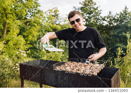 Man seasoning mushrooms on barbecue grill outdoors, summer picnic cooking Man seasoning mushrooms on barbecue grill outdoors, summer picnic cooking 136451093
