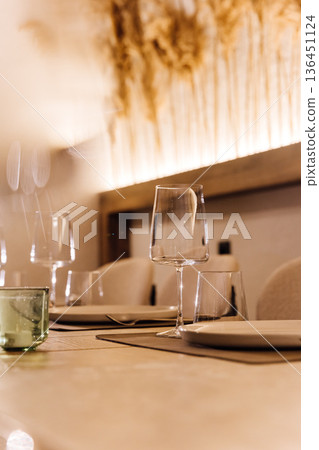 Wine glass on set restaurant table with warm candlelight and pampas decor 136451124