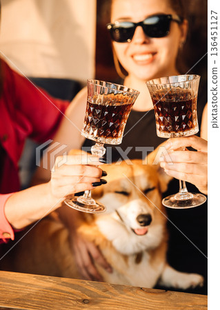 Close up toast with crystal glasses and corgi on sunny outdoor terrace 136451127