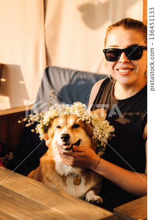 Woman in sunglasses holding corgi in flower crown, golden hour portrait Woman in sunglasses holding corgi in flower crown, golden hour portrait 136451133