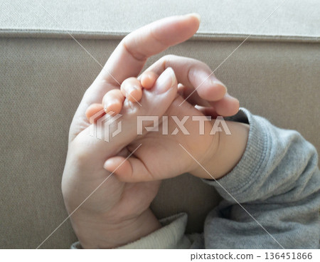 Close-up of baby's hand holding parent's finger on sofa 136451866