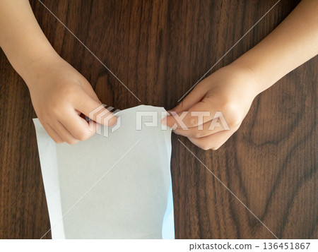 孩子的手在木桌上折淺藍色的摺紙。 136451867