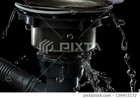 Drain sink leak water from pipe plumbing in bathroom as water splash clogged drop. Pouring Leaking water from gray plastic pipe drain sink. Black background isolated 136453172