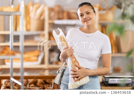 Middle-aged woman holding baguettes in paper bag in bakery Middle-aged woman holding baguettes in paper bag in bakery 136453638