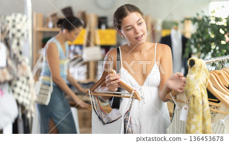 Girl customer choose something clothing for summer. Female client looking for clothes in background Girl customer choose something clothing for summer. Female client looking for clothes in background 136453678