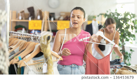 Near rack, asian woman buy summer clothes, choose some items. Female client looking for something in background 136453679